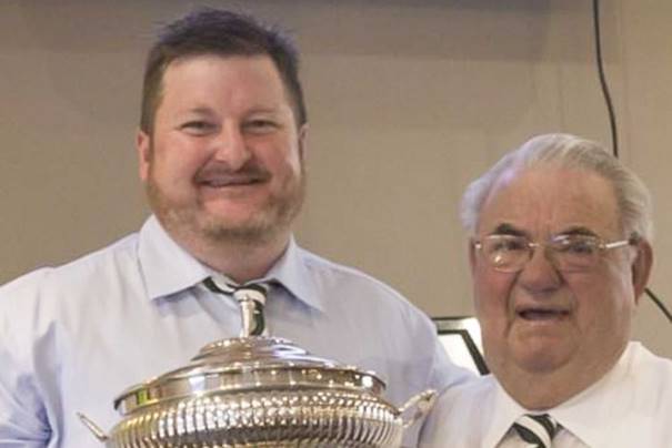 Picture of a younger man holding a silver trophy with an older man