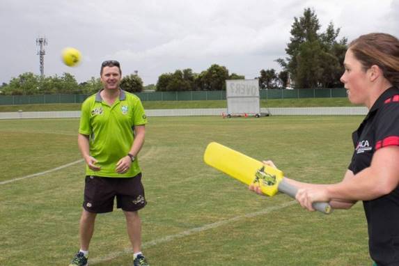 A cricket NSW development officer in a green T20 blast about to take a catch from a woman holding a yellow bat 
